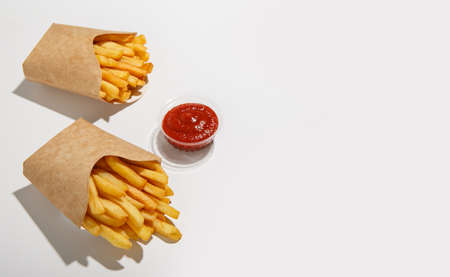Client order and fast food home delivery. French fries in eco carton packing and tomato ketchup in plastic container with shadow, isolated on white background, flat lay, panorama, copy spaceの写真素材
