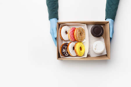 Coffee with sweets for two takeaway during covid outbreak. Waiter in rubber gloves gives box of...