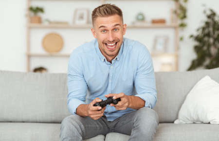 Online Competition Concept. Portrait of excited young man playing video games, holding console...