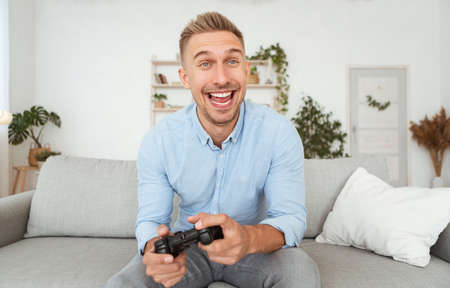 Fun Hobby For Singles Concept. Overjoyed guy playing online video games, holding joystick in hands....