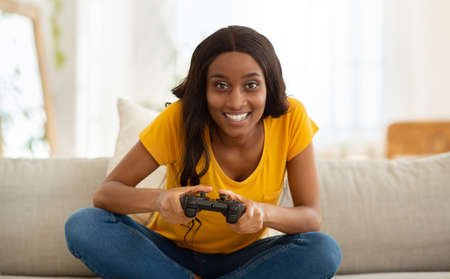 Having fun at home. Happy black woman with controller playing online video games indoors, panorama....