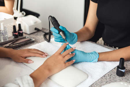 Modern manicure in salon, hygiene and social distancing. African american woman with rubber gloves filing nails with electric tool at table with equipment, close up, cropped, free spaceの写真素材