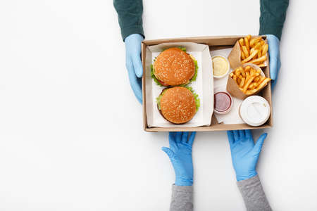 Fast food for two during coronavirus epidemic. Waiter hands in protective gloves gives box with...