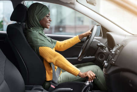 New Transport. Happy Black Islamic Lady In Hijab Driving Modern Car, Sitting On Drivers Seat,...