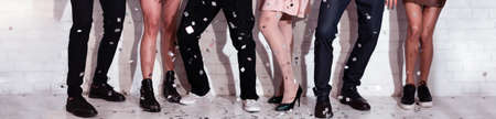 Party Concept. Legs Of Unrecognizable Group Of People Celebrating Holiday With Confetti Dancing Standing Against White Wall Indoor. Panorama, Croppedの写真素材