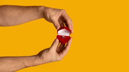 Male hands holding box with beautiful engagement ring on orange background, copy space. Panorama