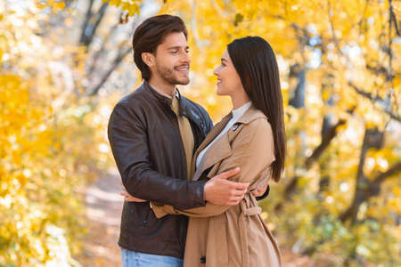 Beautiful couple in love embracing and looking at each other while walking by autumn forest, copy...