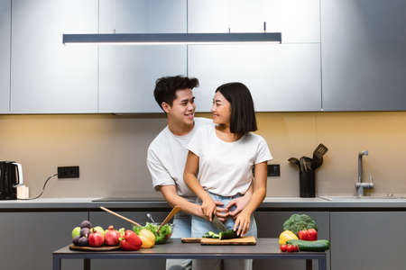 Dating Asian Couple Cooking Together Making Veggie Salad For Dinner Hugging In Modern Kitchen At Home. Preparing Food For Weekend Date. Tasty Meals Recipes And Family Nutrition Conceptの写真素材