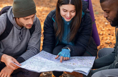 Multiracial friends backpackers looking at map, hiking in autumn forest, closeup