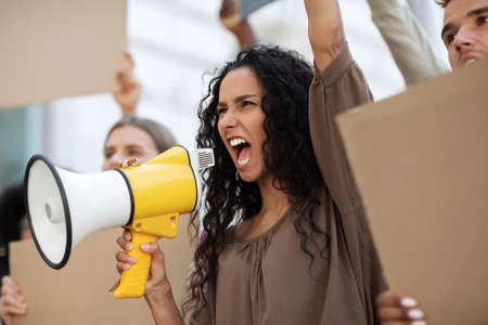 Active mixed race woman with megaphone leading public meeting on the street. International group of young people holding empty placards, protesting against discrimination or racism, closeupの写真素材