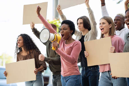 Multiethnic young demonstrators striking on the street, holding megaphone and empty placards....