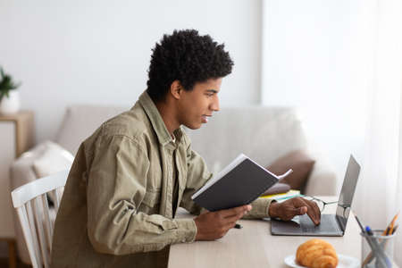 Remote education concept. Side view of black teenage student with notebook participating in web...