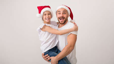 Father in santa hat carrying daughter on hands, white studio background, panorama