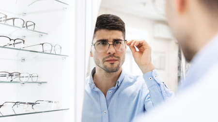 Choosing Glasses Concept. Over the shoulder portrait of handsome bearded guy picking new eyewear at...