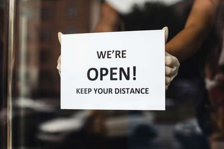 Reopening store or beauty salon after quarantine and new normal. Hands in rubber gloves hang up notices on glass door or showcase, we are open, keep your distance, free space, croppedの写真素材