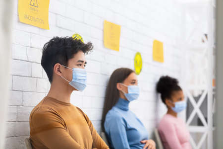Diverse People Waiting For Coronavirus Vaccination Sitting In Queue In Hospital Waiting-Room, Wearing Medical Masks. Covid-19 Vaccine For Population Campaign, Corona Virus Prevention And Treatmentの写真素材