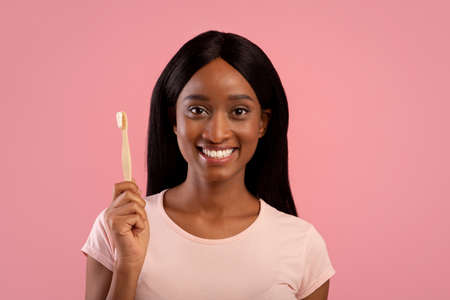 Portrait of beautiful African American woman with radiant smile holding wooden toothbrush with paste...