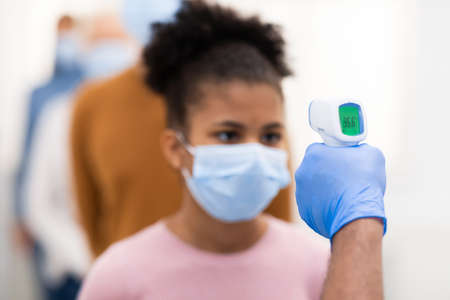 Medical Worker Doing Temperature Screening For Teen Girl And People Standing In Queue, Measuring...
