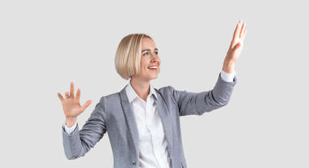 Beautuful Caucasian businesswoman interacting with virtual screen on light studio background, space for design. Smart female entrepreneur touching imaginary display, panoramaの写真素材