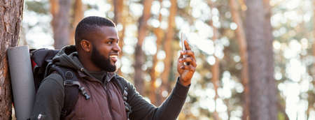 African man backpacker with smartphone in forest, happy to get connection, panorama with copy spaceの写真素材