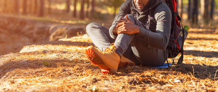 Cropped of black man sitting on ground and rubbing his injured knee, panorama with copy spaceの写真素材