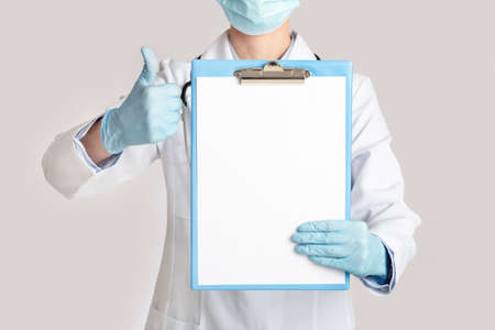 Excellent results, convalescence, diagnostics and treatment. Female doctor in protective mask, white coat and rubber gloves showing thumbs up and tablet for examination with blank space, croppedの写真素材