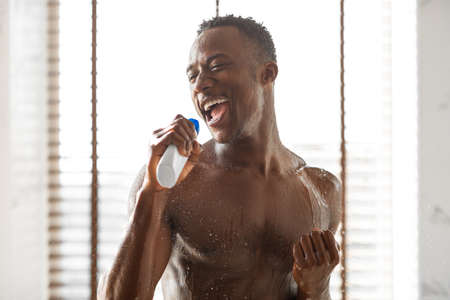 Funny Black Guy Singing Taking Shower Relaxing And Having Fun Standing Under Falling Water Drops, Relaxing In Bathroom At Home. Enjoy Hygiene Routine, Male Bodycare Conceptの写真素材
