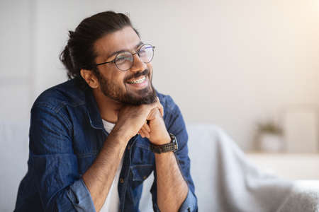 Portrait Of Smiling Indian Man With Eyeglasses And Braces In Home Interior, Handsome Pensive Western Guy Daydreaming And Looking Away, Thinking About Something, Selective Focus With Copy Spaceの写真素材