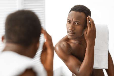 Dandruff Hair Problem. Black Man Looking In Mirror Examining Head Having Male-Pattern Baldness Issue Standing In Modern Bathroom Indoors. Mens Haircare Treatment Concept. Selective Focusの写真素材