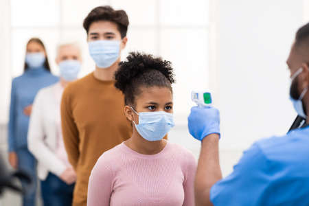 Temperature Screening Concept. Nurse Measuring Fever For Black Patient Girl Standing In Queue Line,...