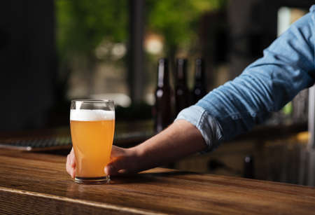 Oktoberfest in pub. Bartender hand holds lager beer in glass in interior of bar, close up, free space, croppedの写真素材