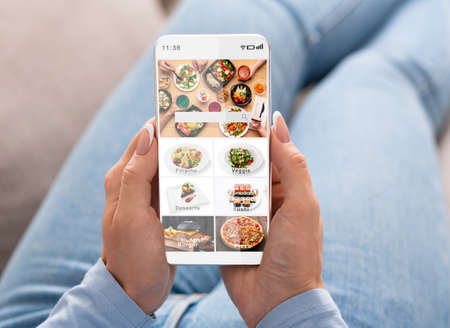 Ordering food at home using mobile application during pandemic covid-19. Woman surfing at online restaurant and chooses meal in menu with delivery, and look at screen, pov, close up, free spaceの写真素材