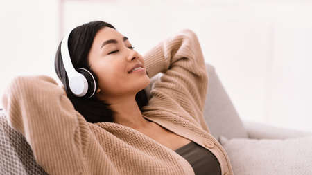 Rest And Relax Concept. Closeup portrait of calm asian woman lying on couch, listening to music, audio book, podcast, enjoying meditation for sleep and peaceful mind in wireless headphones, copy spaceの写真素材