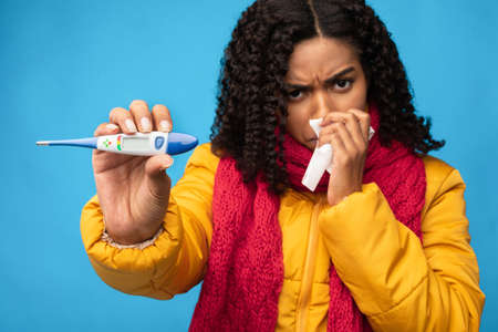 Sick Black Woman Showing Thermometer Having Fever Standing Over Blue Studio Background, Wearing...