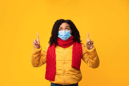 Look There. Black Woman In Coronavirus Face Mask Pointing Fingers Up Standing Over Yellow Studio...
