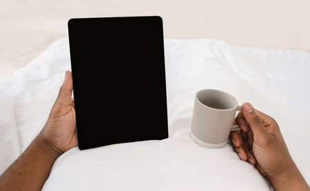 Black Male Hands Holding Digital Tablet With Empty Screen Reading E-Book Online Lying In Bed At Home, Enjoying Morning Coffee. Application Advertising, Weekend Leisure. Cropped, Mockup, POVの写真素材