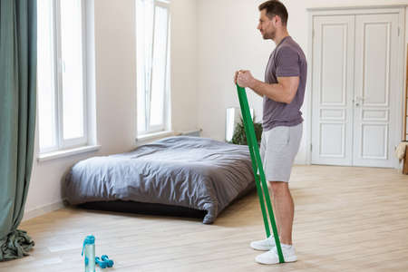 Home Fitness. Man Exercising Using Resistance Rubber Band Loop Training In Bedroom Indoors In The...