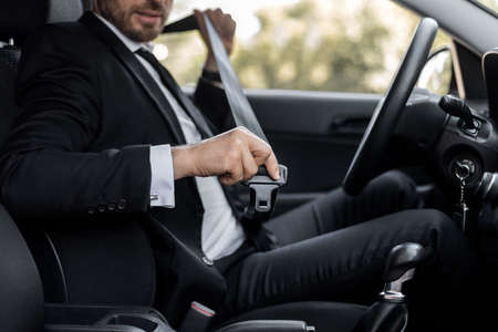Driving safety concept. Unrecognizable businessman fasten seat belt in his car, ready to go to...