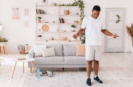 African American Guy Holding Jumping Rope Exercising Standing At Home. Morning Physical Training...