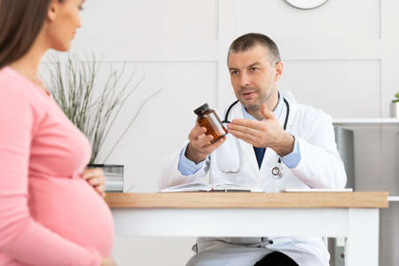 Pregnancy and Medication Concept. Doctor Prescribing Pills For Pregnant Woman During Appointment In Office, Holding And Showing Drugs Or Vitamin. Gynecology, Medicine, Health Care And People.の写真素材