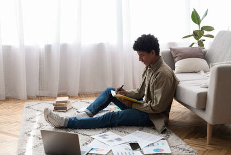 African American teenage student taking notes for complicated exam during remote studies at home, copy space. Handsome black guy working on his home assignment, writing paper or educational projectの写真素材
