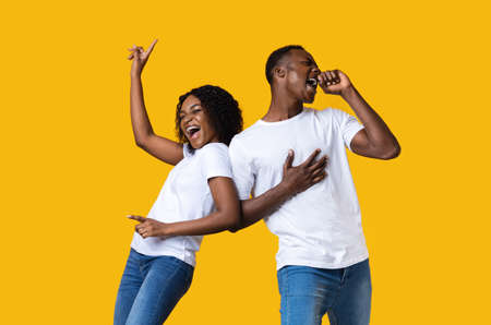 Emotional black man and woman dancing and singing on yellow studio background with copy space. Joyful african american lovers having fun together, listening to music, moving and screamingの写真素材