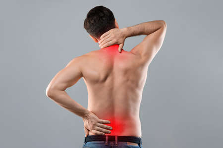 Man holding his hands behind his back, pain in spine, inflamed zones highlighted in red, grey studio...