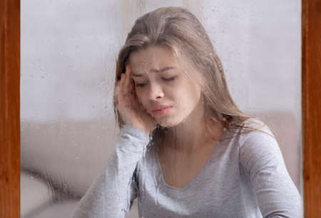 Seasonal affective disorder concept. Young woman feeling depressed, looking out window at autumn...