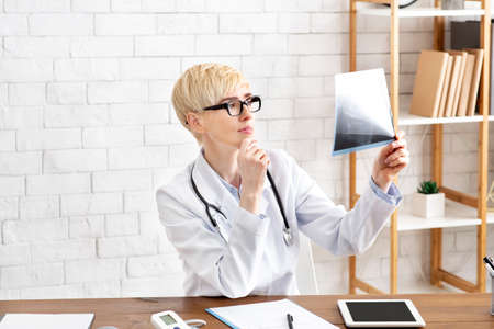 Work of medical specialist and diagnostics. Serious middle aged lady doctor in glasses in white coat...