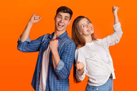 Success, dance and victory. Happy guy and lady in casual clothes celebrate winning, raise their fists up and express emotions of fun, isolated on orange background, studio shot, free space, cut outの写真素材