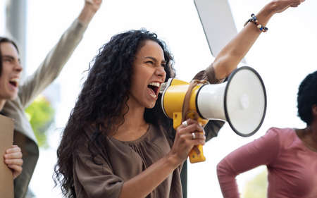 Closeup of motivated young woman with loudspeaker leading international group of strikers,...