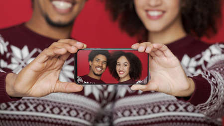 Focus on smartphone with selfie of smiling african american man and lady on screen in hands of...