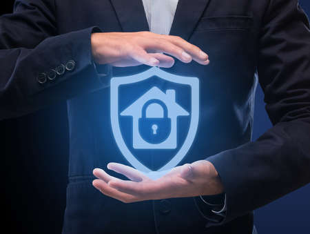 Home Security System And Protection Concept. Man in suit holding hologram of locked house icon in hands. Modern Technology For Surveillance And Remote Control. Internet Of Things And Safetyの写真素材