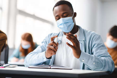 Hygiene And Health Concept. African american man student applying antibacterial sanitizer on hands,...